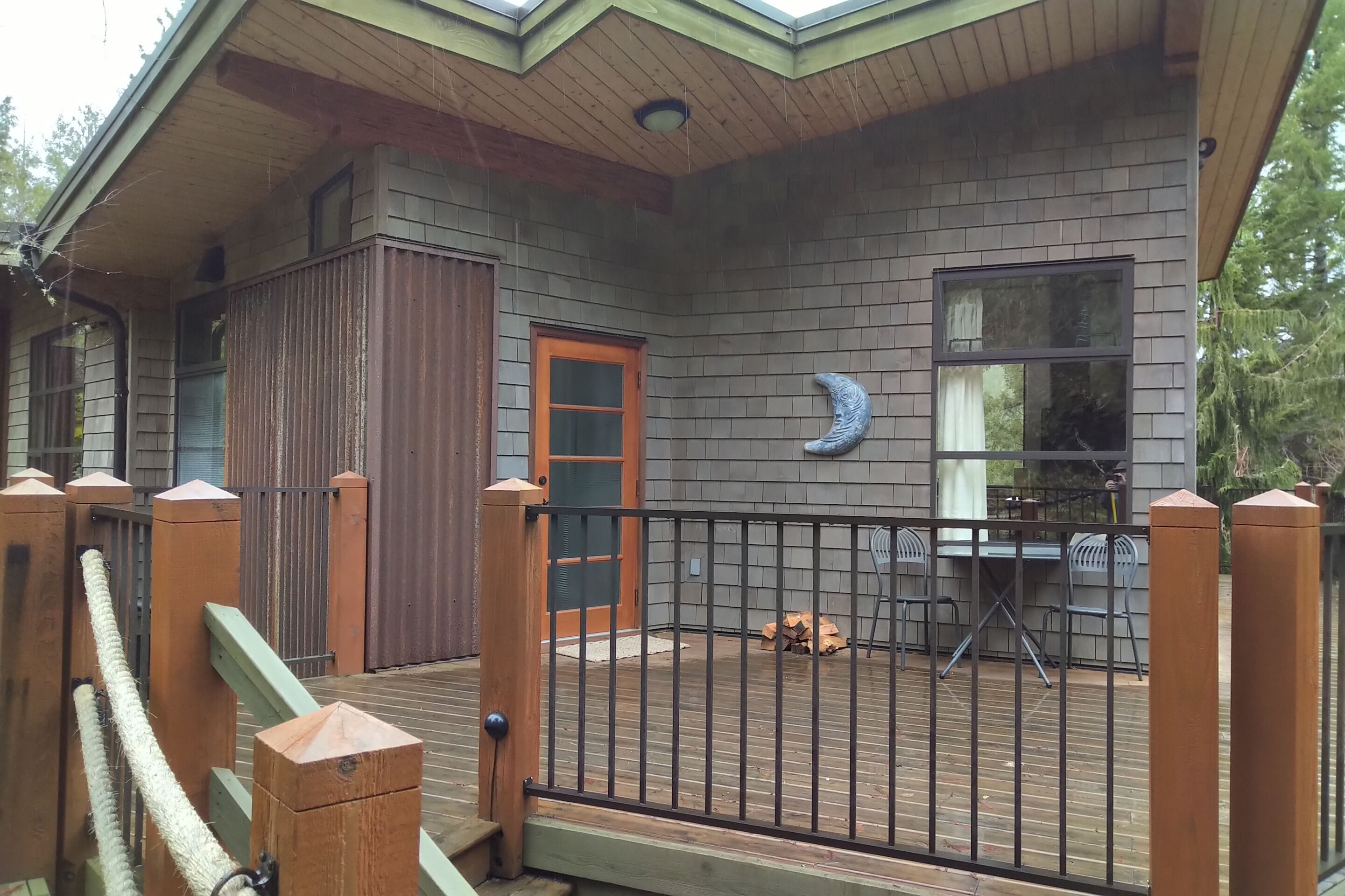 A wooden deck with a metal fence, a door, and a window with a moon decoration.