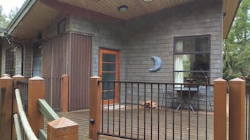 A wooden deck with a metal fence, a door, and a window with a moon decoration.