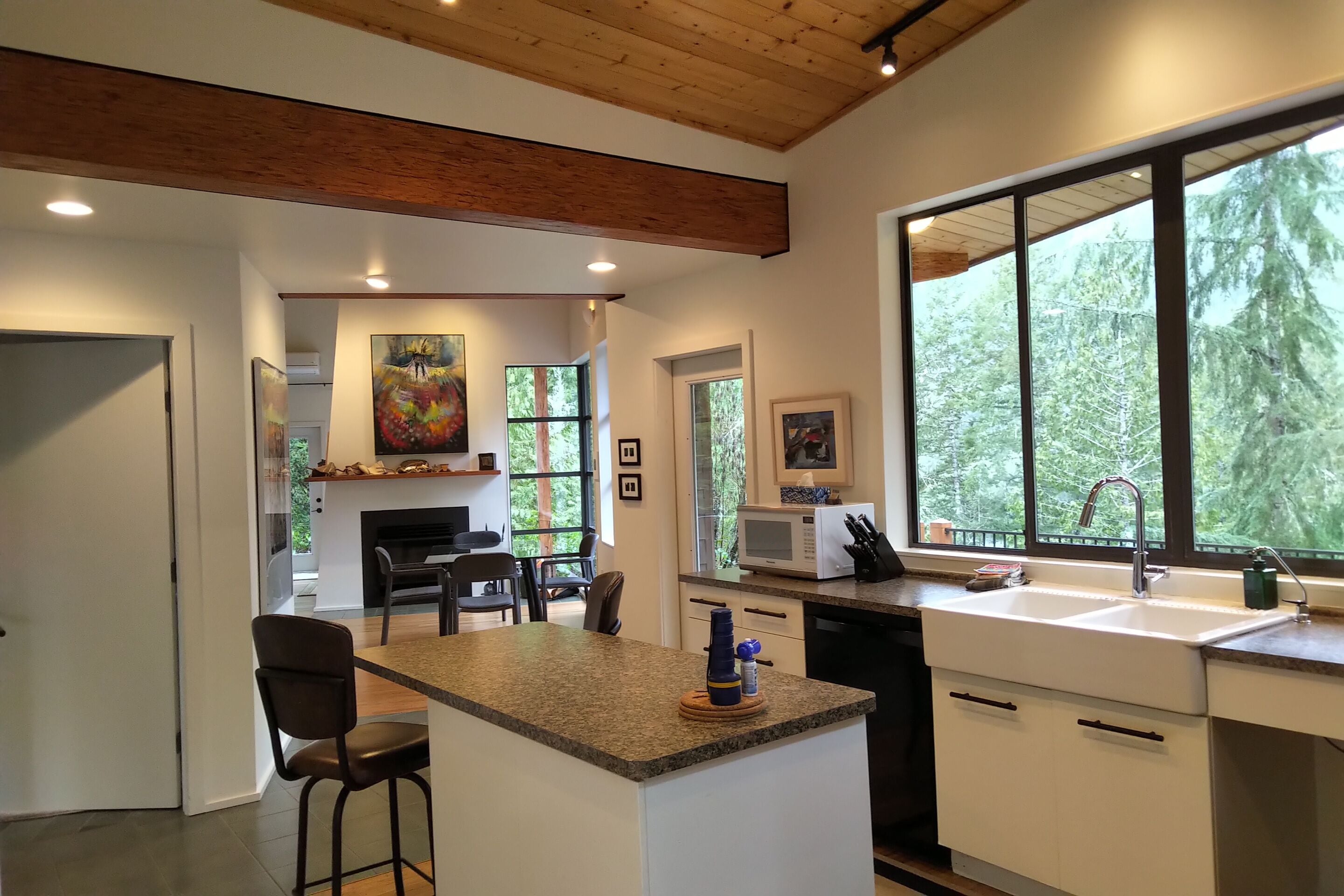 A modern kitchen with a central island, a dining area with chairs, and large windows offering a view of the outdoors.