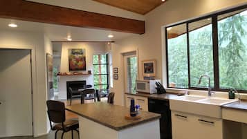 A modern kitchen with a central island, a dining area with chairs, and large windows offering a view of the outdoors.