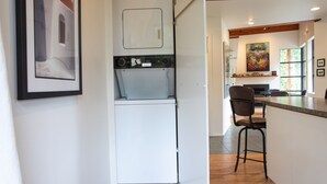 Een compacte keuken met een ingebouwde wasmachine en droger, een houten plafond en een eethoek met een bargedeelte.
