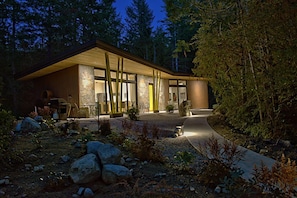 A modern house with a large wooden structure, a stone wall, and a pathway leading to the entrance. - Modern Forest Guest Suite - Accessible Seclusion! (Madeira Park)
