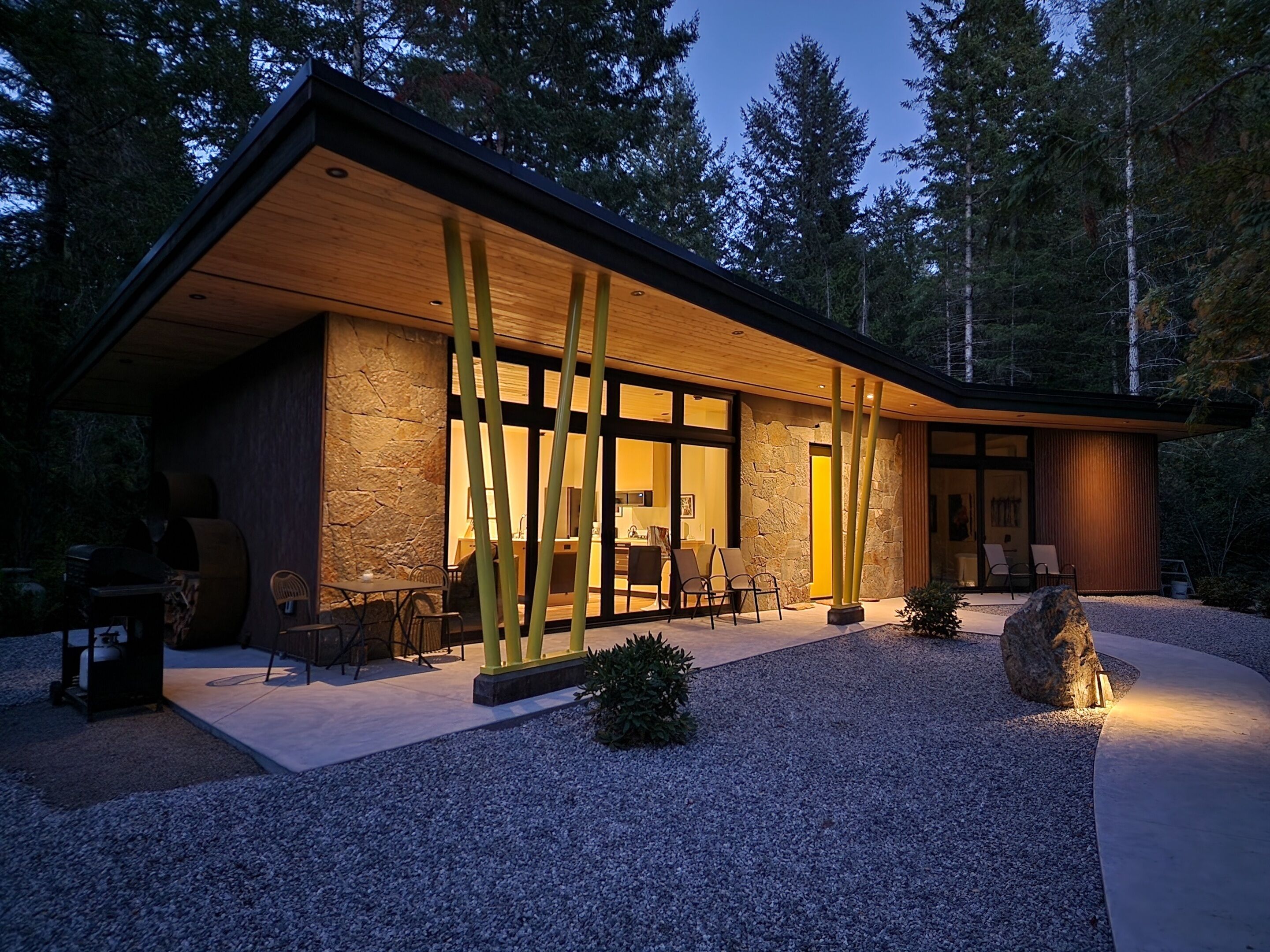 A modern house with a stone facade, large windows, and a covered outdoor seating area.