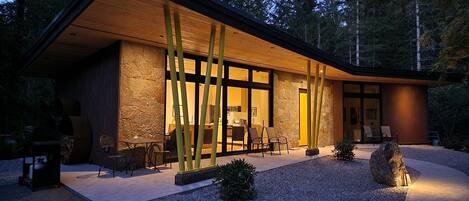 A modern house with a stone facade, large windows, and a covered outdoor seating area.
