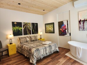 A bedroom with a bed, bedside tables, a chair, a painting, and a bathroom with a bathtub.