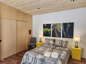 Ein Schlafzimmer mit Holzboden, einem Bett mit gemustertem Überwurf, zwei Nachttischen mit Lampen und drei an der Wand befestigten Bildern.