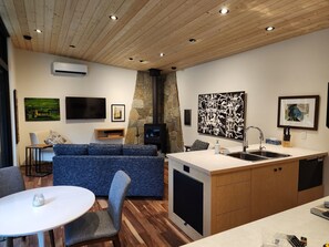 A modern kitchen with a built-in stove, a sink, and a dining area with a white table and blue upholstered chairs.