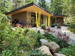 Ein modernes Gebäude mit Holzfassade und großen Fenstern, umgeben von einem Garten mit verschiedenen Pflanzen und Steinen.