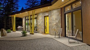 A modern building with a stone facade, large glass doors, and a well-lit outdoor seating area. - Modern Forest Guest Suite - Accessible Seclusion! (Madeira Park)