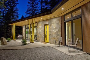 Ein modernes Haus mit Natursteinfassade, großen Glasüren und einer Holzterrasse.