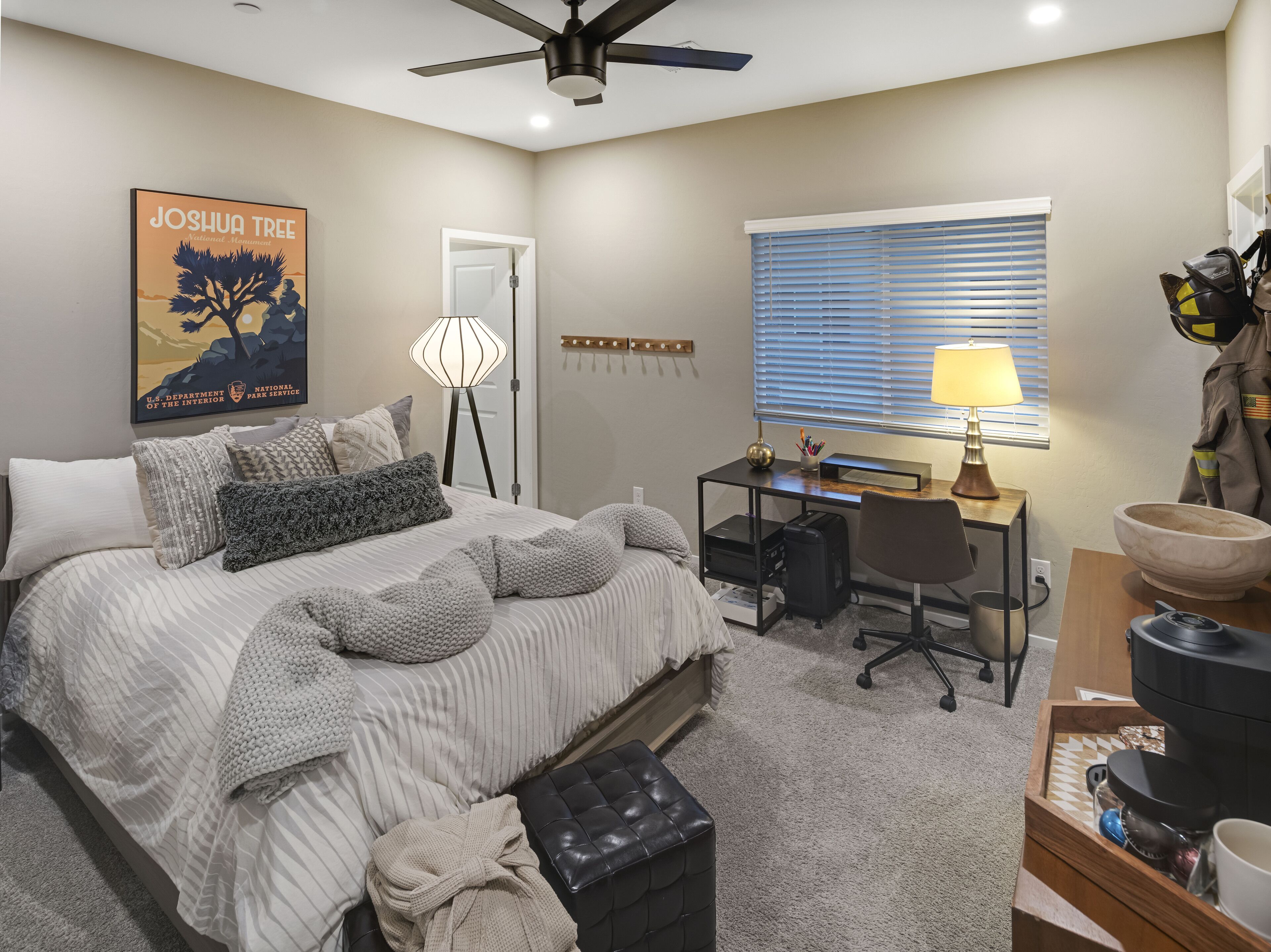 A bedroom with a bed, desk, chair, and a ceiling fan.