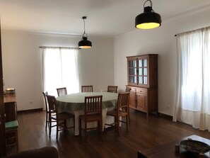 A dining area with a round table, wooden chairs, a cabinet, and two pendant lights. - Casa do Monte - Garden & Sea sight (Caloura)