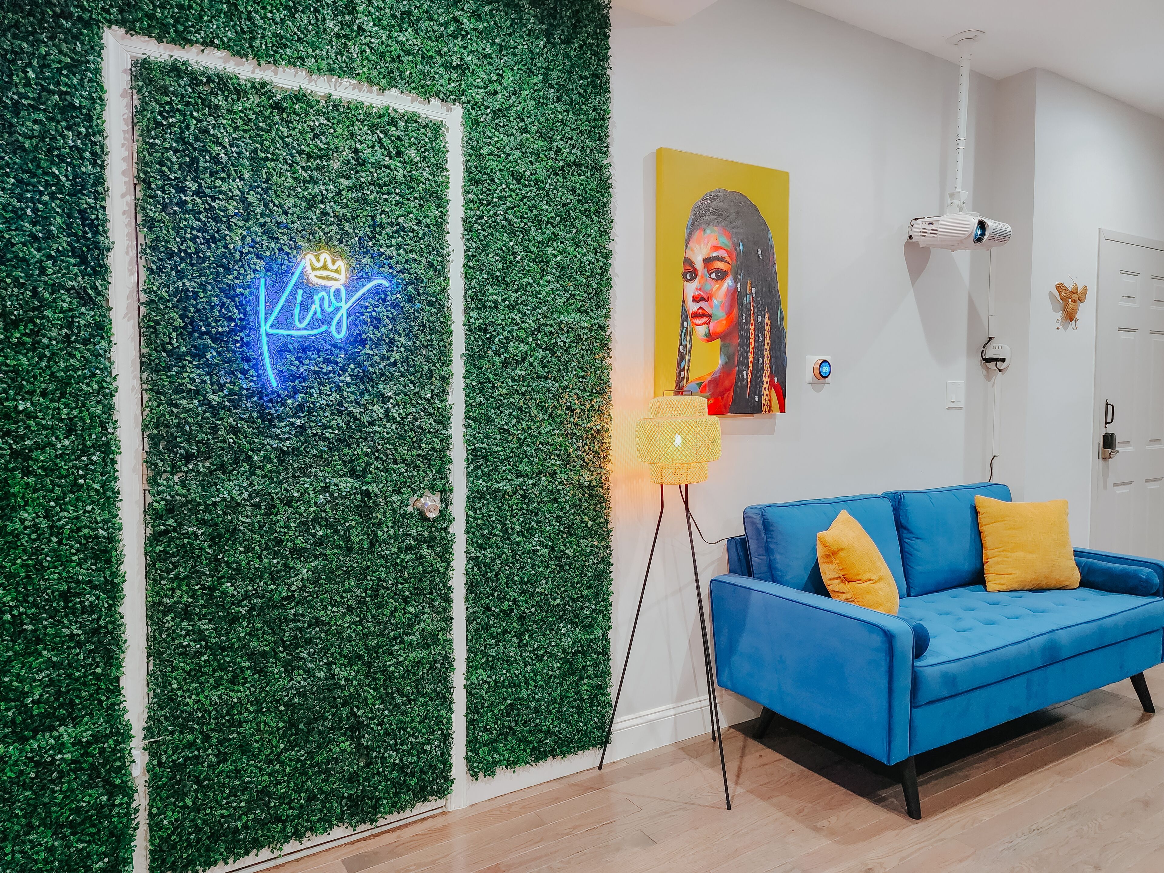 Una habitación con un sofá azul, un letrero de neón, un cuadro y un proyector.
