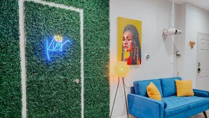Ein Zimmer mit einem blauen Sofa, einer Neonreklame, einem Gemälde und einem Projektor.