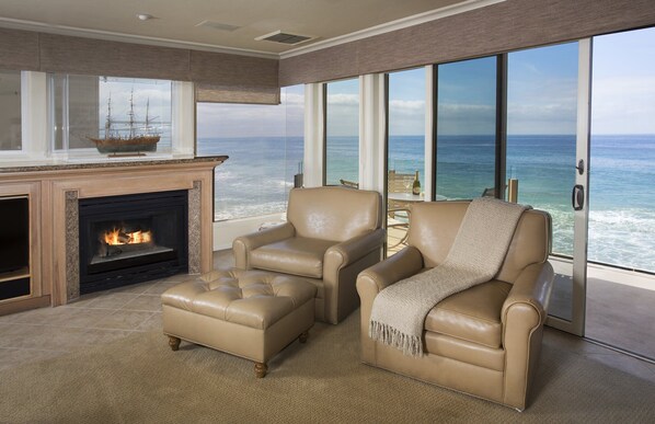 Una sala de estar con chimenea, dos sillones de cuero, una mesa de centro de vidrio y vistas al océano.