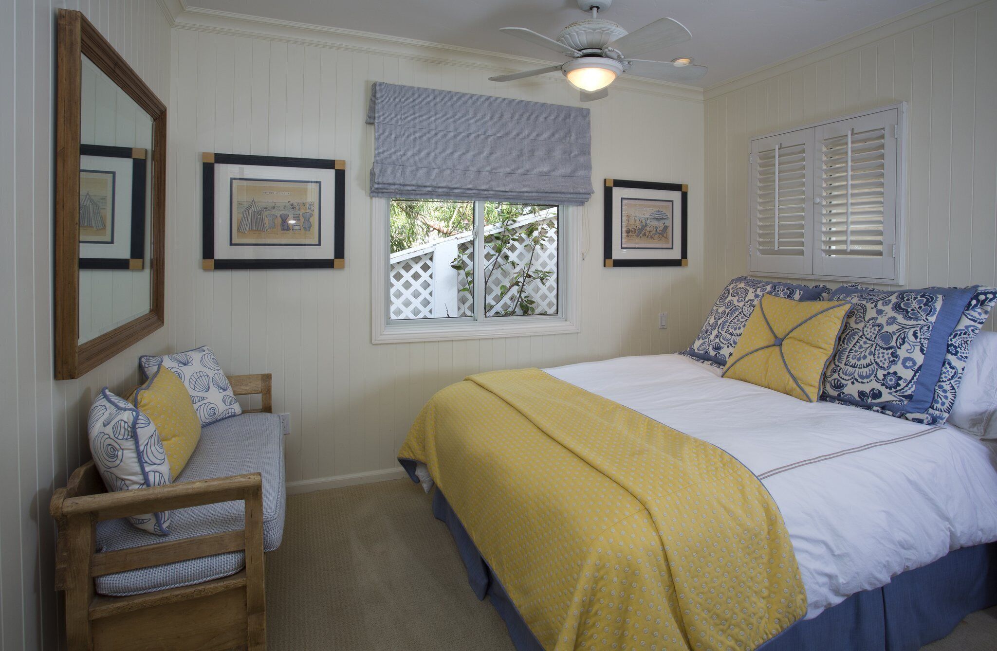 A bedroom with a bed, a chair, a window with blinds, and framed pictures on the wall.