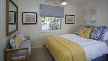 A bedroom with a bed, a chair, a window with blinds, and framed pictures on the wall.