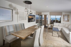 Un salón moderno con una mesa de comedor de madera, un sofá a rayas y vistas al océano a través de grandes ventanales.
