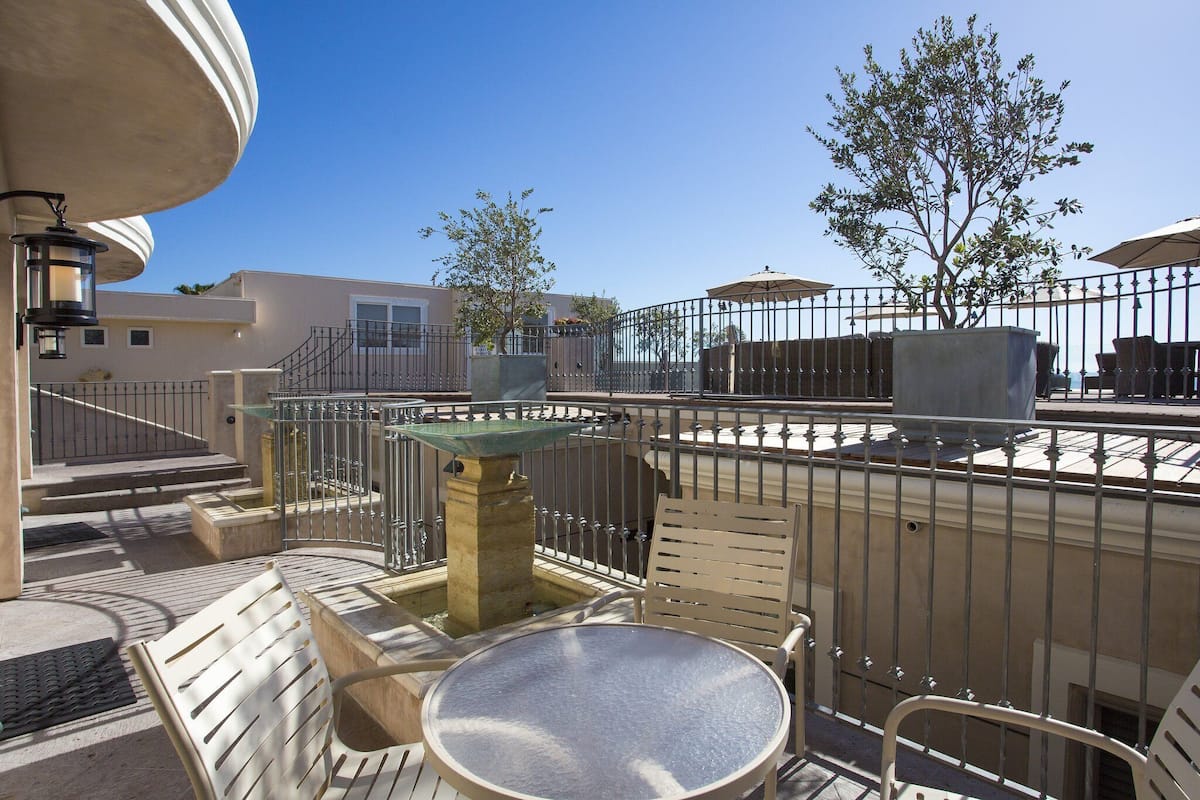 Une terrasse extérieure avec une table ronde et des chaises, une fontaine en pierre et, en arrière-plan, une vue sur un bâtiment.