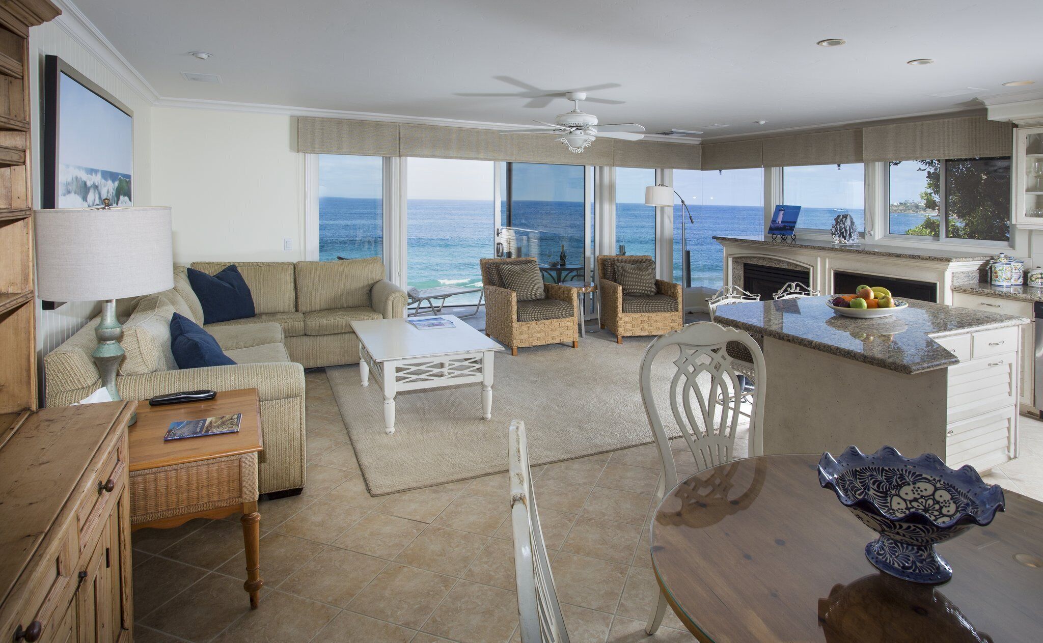 A spacious living area with a sofa, chairs, a coffee table, and a dining table. There is a kitchen area with a stove and a view of the ocean through large windows.
