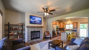 A spacious living room with a fireplace, a television mounted above it, and a modern kitchen in the background. - Coeur d'Alene Hideaway 4 Bedroom Modern Mid Term Rental (Coeur d'Alene)