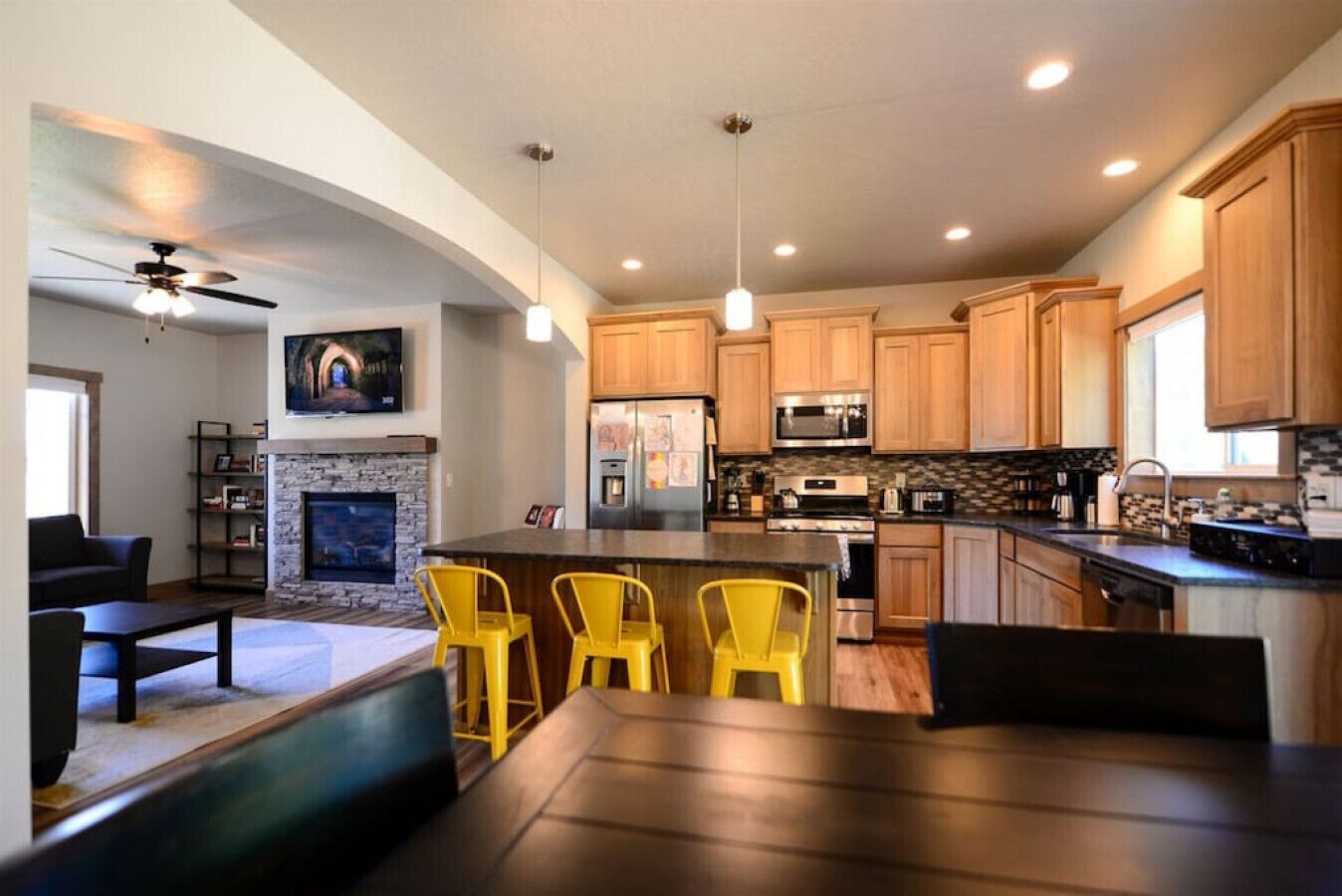 A modern kitchen with wooden cabinets, a central island, and yellow bar stools.