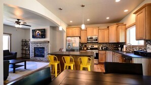 A modern kitchen with wooden cabinets, a central island, and yellow bar stools. - Coeur d'Alene Hideaway 4 Bedroom Modern Mid Term Rental (Coeur d'Alene)
