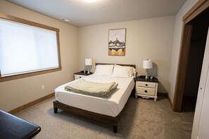 A bedroom with a bed, two bedside tables with lamps, a window with blinds, and a wall-mounted picture. - Coeur d'Alene Hideaway 4 Bedroom Modern Mid Term Rental (Coeur d'Alene)