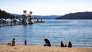 A lakeside beach with a pier, a lighthouse, and a row of beach umbrellas. - Coeur d'Alene Hideaway 4 Bedroom Modern Mid Term Rental (Coeur d'Alene)