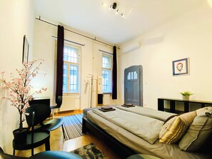 A bedroom with a bed, a desk, a chair, a radiator, a window, a door, and a plant. - Huge family friendly 2br Central Apartment with A/C, crib - Deco House (Budapest)