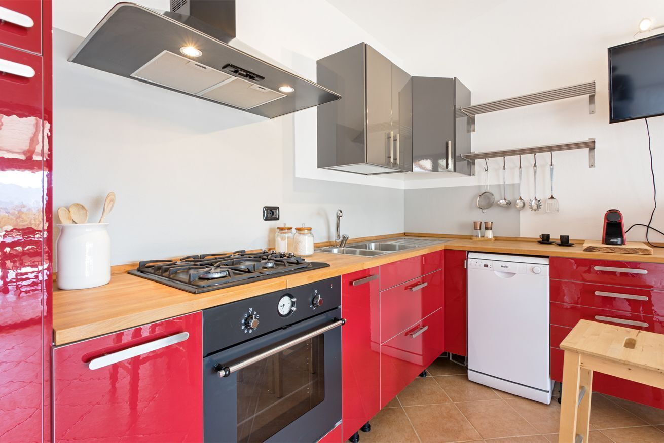 Une cuisine moderne avec des meubles de rangement rouges, une cuisinière à gaz, un four, un lave-vaisselle et un plan de travail en bois.