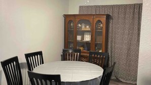 Une salle à manger avec une table ronde, six chaises, un ventilateur de plafond et un buffet en bois doté de portes en verre.