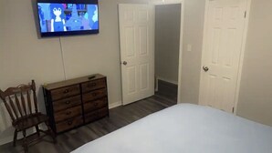 Une chambre à coucher avec un lit, une commode en bois, une chaise et un téléviseur diffusant un dessin animé japonais.