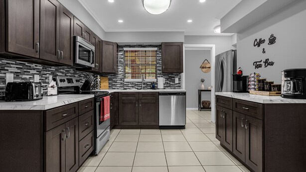 A modern kitchen with dark wood cabinets, stainless steel appliances, and a tiled backsplash. - Home Paradise Lakeland Heated Pool • Jacuzzi • BBQ Backyard (Lakeland)