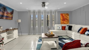 A modern living room with a white sofa, a coffee table, and a large painting on the wall. - Home Paradise Lakeland Heated Pool • Jacuzzi • BBQ Backyard (Lakeland)