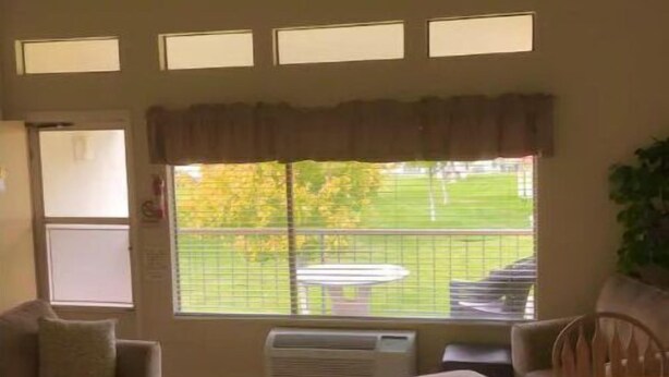 A living room with a sofa, ottoman, and a dining table. There are large windows with a view of a green outdoor area. - #108 Condo near large pool & shuttle to Gorge Amp-book separately (Quincy)