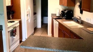 A compact kitchen with wooden cabinets, a white refrigerator, a stove, and a sink. There are two stools at the counter. - #108 Condo near large pool & shuttle to Gorge Amp-book separately (Quincy)