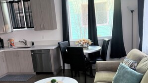 Una sala de estar moderna con un sofá color beige, una mesa de centro redonda y un comedor con una pequeña mesa y sillas.