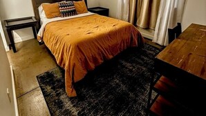 Una habitación de hotel con cama, ventilador de techo, ventana con cortinas y una mesita.