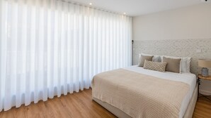 Une chambre avec un grand lit, des rideaux blancs, un plancher en bois et un mur orné de motifs.