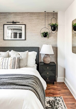 Een slaapkamer met een bed, nachtkastje, lamp en wandplanten.