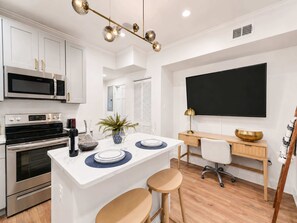 A modern kitchen with a central island, built-in appliances, and a flat-screen TV mounted on the wall.