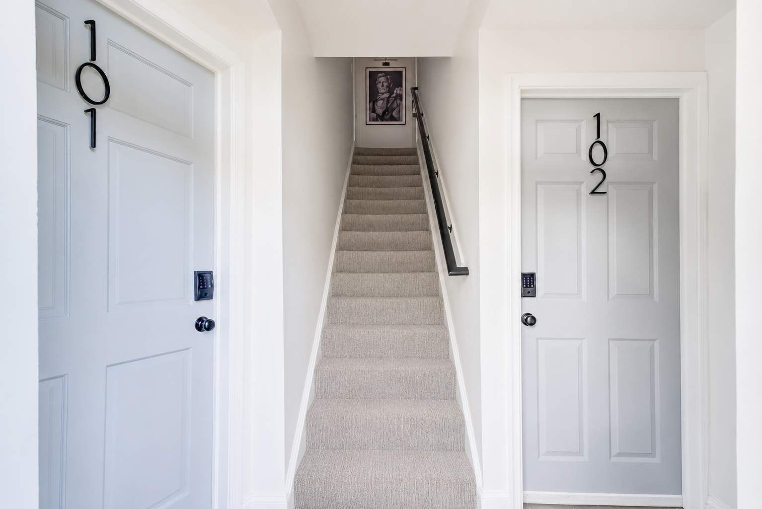 Un couloir avec deux portes, portant les numéros « 101 » et « 102 », qui donnent sur un escalier recouvert de moquette.