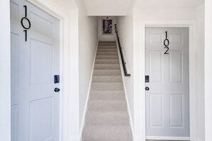 Un pasillo con dos puertas, identificadas con los números '101' y '102', que dan a una escalera con alfombra.