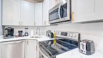 A modern kitchen with white cabinets, a built-in microwave, a stove, a toaster, and a coffee maker.