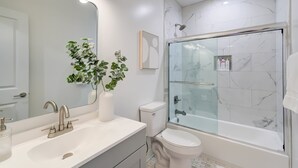 A modern bathroom with a large mirror, a white sink, a toilet, and a glass-enclosed shower. - Lincoln Lofts: 202 | Bright & Stylish DC Retreat (Washington)