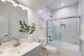 Een moderne badkamer met een grote spiegel, een witte wastafel, een toilet en een douchecabine met glazen wanden.