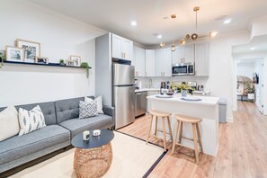 A modern kitchen with white cabinets, a stainless steel refrigerator, and a central island with stools. - Lincoln Lofts: 202 | Luxe Boho 2BR in Heart of DC (Washington)
