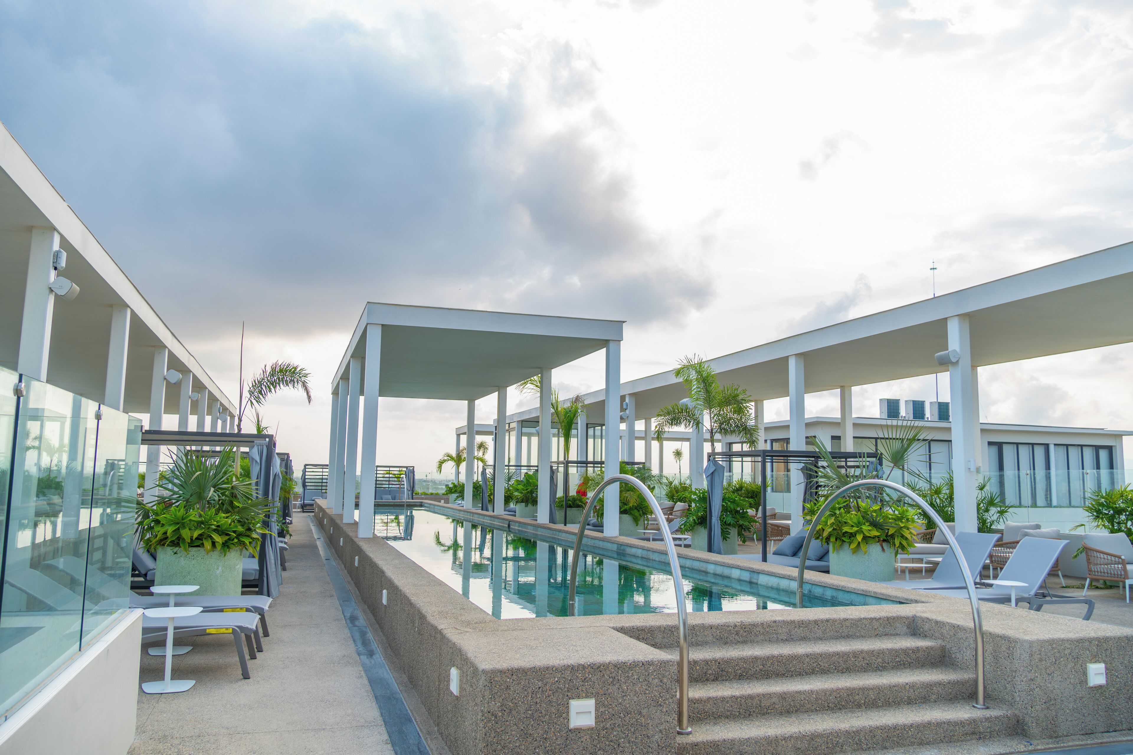 Área de piscina en la azotea con sillones de descanso, piscina y barandilla de vidrio.