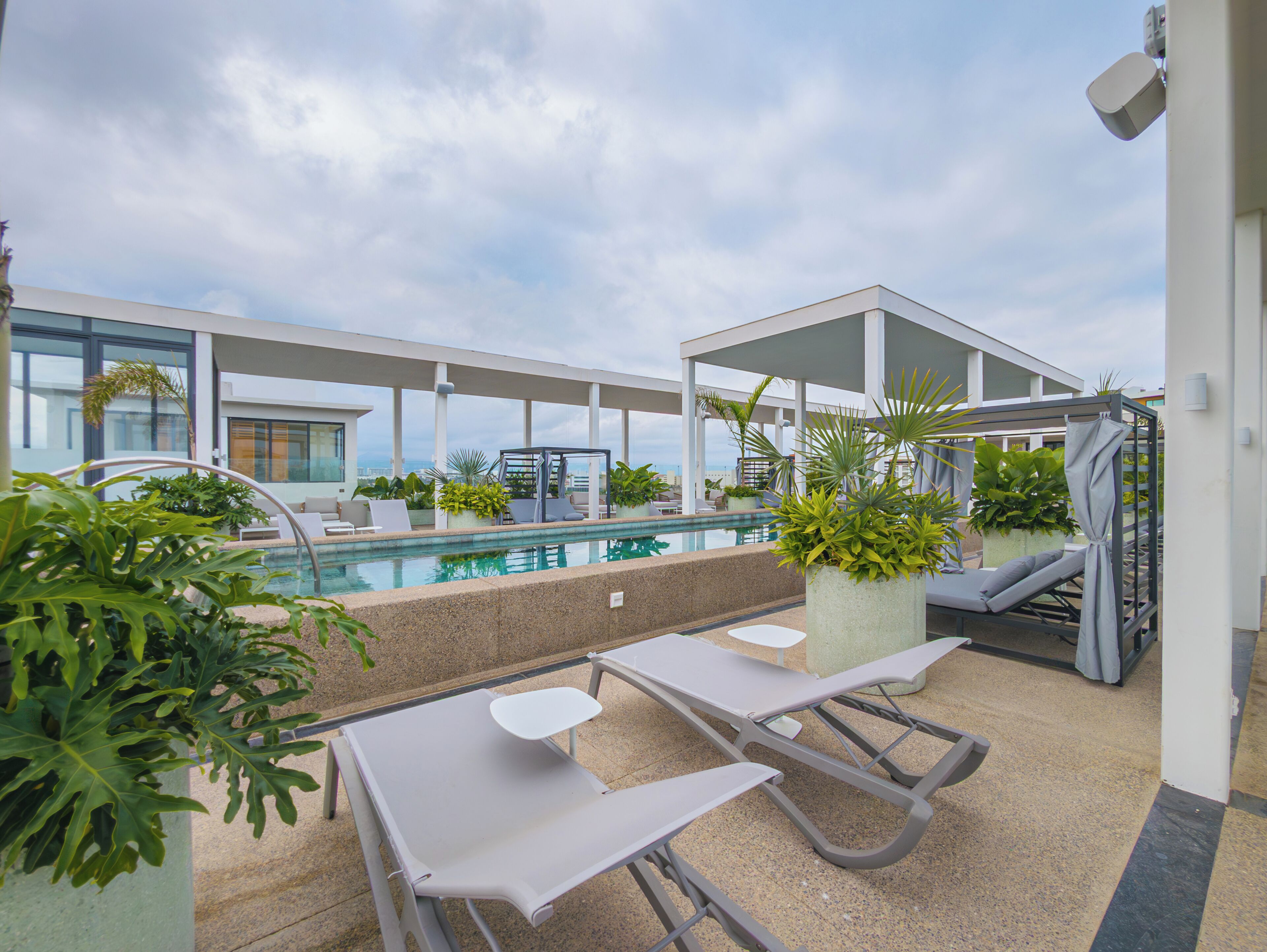 A rooftop pool area with lounge chairs, planters, and a view of the city.